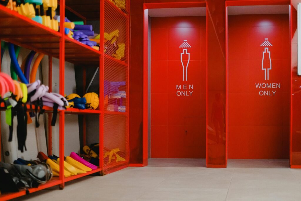 Colorful pool gear in storage beside gender-specific showers with vibrant red decor.